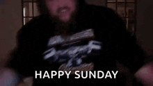 a man in a black shirt is dancing in a dark room with the words `` happy sunday '' written on the screen .