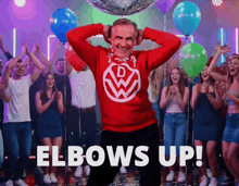 a man wearing a red sweater with a volkswagon logo is dancing in front of a disco ball and balloons
