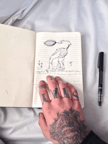 a person with tattoos on their fingers is holding a notebook with a drawing on it