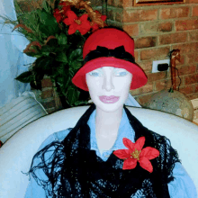 a mannequin wearing a red hat and a black scarf has a red flower pinned to her chest