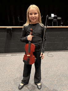 a young girl is holding a violin and smiling at the camera