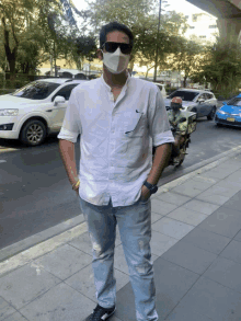 a man wearing a face mask and sunglasses stands on a sidewalk