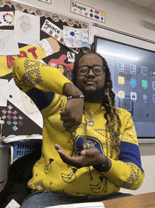 a man wearing a yellow sweater with bananas on it is sitting in front of a bulletin board that says shape