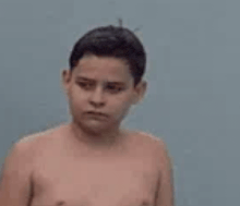 a shirtless young boy is standing in front of a wall .