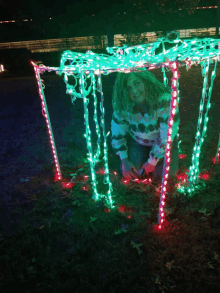 a woman is kneeling down in front of a christmas light display