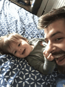 a man with a beard is laying on a bed with a baby who is wearing a shirt that says mickey mouse