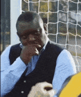 a man wearing a blue shirt and black vest is sitting in front of a soccer net