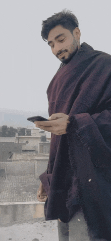 a man wearing a purple poncho is looking at his cell phone