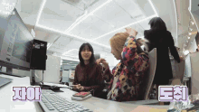 two women are sitting at a desk with a keyboard and a computer monitor with twice written on the bottom right corner