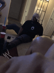 a man wearing a black shirt with the letter o on it sits on the floor in a living room