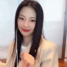 a woman with long black hair is wearing a white shirt and a tan jacket .