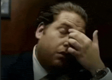 a man in a suit and tie is rubbing his nose with his hand .