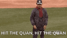 a man is dancing on a baseball field with the words `` hit the quan , hit the quan '' behind him .