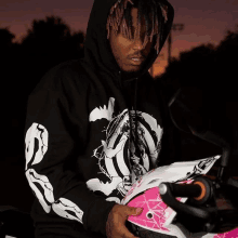 a man wearing a black hoodie holds a pink helmet