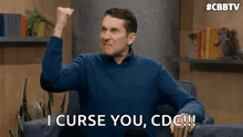 a man is sitting in a chair with his fist in the air and saying `` i curse you , cdc !! ''