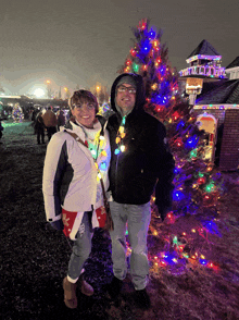 a couple standing in front of a christmas tree