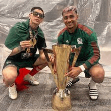 two men are kneeling down next to a trophy and drinking from it .