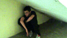 a young boy squatting down in a corner with his arms crossed