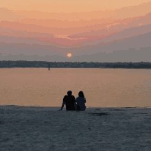 two people sit on the beach watching the sun set