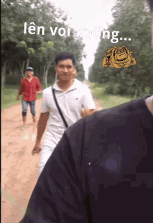 a man in a white shirt is walking down a dirt road with the words len voi xuong above him