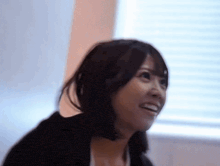 a woman is smiling in front of a window with blinds