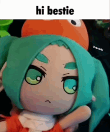 a stuffed doll with green hair and an orange hat is being held by a person and says hi bestie .