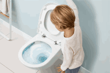 a young boy is looking into a toilet with the lid open