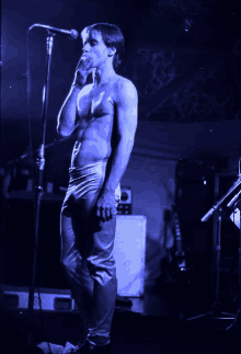 a shirtless man singing into a microphone with a blue light behind him