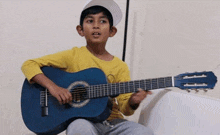 a young boy is playing a blue guitar and wearing a yellow shirt