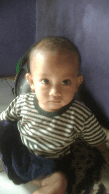 a baby is wearing a striped shirt and sitting on the floor