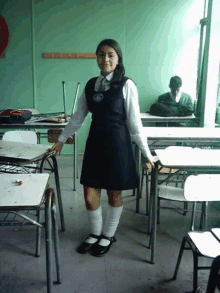 a girl in a school uniform is standing in a classroom with empty desks