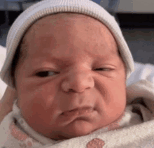 a newborn baby wearing a white hat is making a funny face .