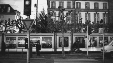 a black and white photo of a street scene with a building in the background and a train going by