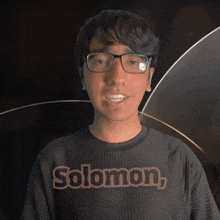 a man wearing glasses and a solomon shirt smiles