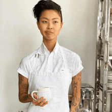 a woman wearing a white apron with kk on it holds a mug