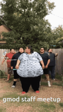 a group of people are standing in front of a wooden fence and one of them has a very large belly