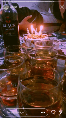 a bottle of black bacardi sits on a table next to glasses