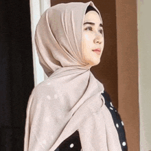 a woman wearing a hijab and a shawl is standing in front of a window .