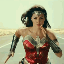 a woman in a wonder woman costume is running down a road with her arms outstretched .