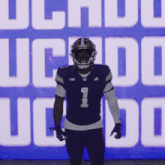 a football player stands in front of a large uc logo