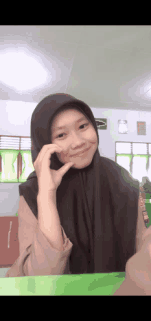 a girl wearing a hijab is smiling and making a peace sign