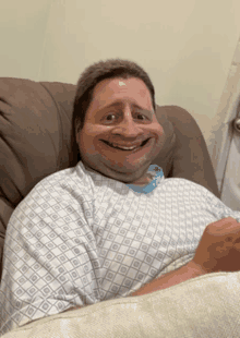 a man in a hospital gown smiles while laying in a chair