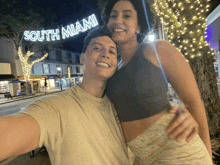 a man and woman are posing for a picture in front of a sign that says south miami