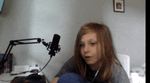 a young girl sitting in front of a microphone with a picture on the wall behind her