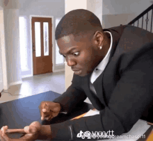 a man in a suit sits at a table looking at a phone