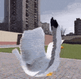a white swan with a yellow beak is flying in the air in front of a building .
