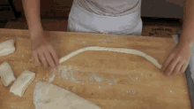 a person is cutting a piece of dough on a wooden table with an apple pie box in the background