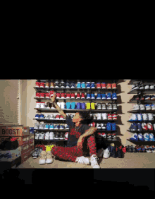 a man sits on the floor in front of a wall of shoes and a picture of a shoe on a computer screen