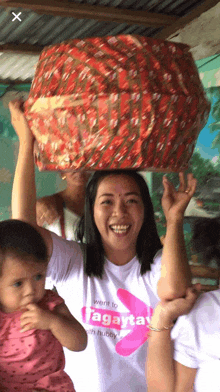 a woman wearing a shirt that says agaytay on it holds a basket on her head