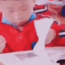 a young boy in a red shirt is sitting at a table with a piece of paper in front of him